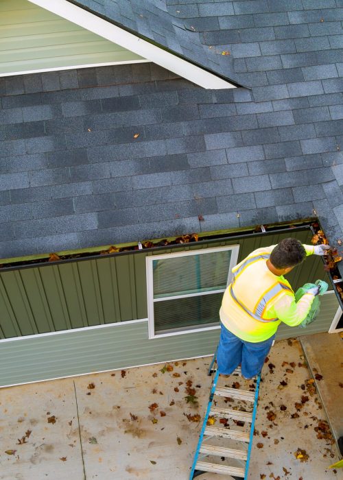 Worker is cleaning clogs in roof gutter drain by picking up dirt, debris, fallen leaves