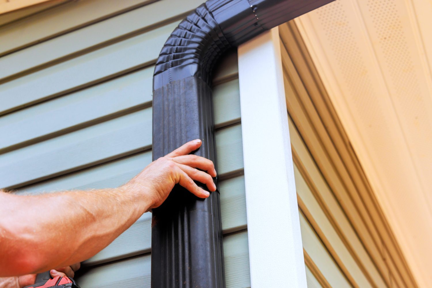 On roof, worker is installing rain gutter fitting downpipe downspout bend