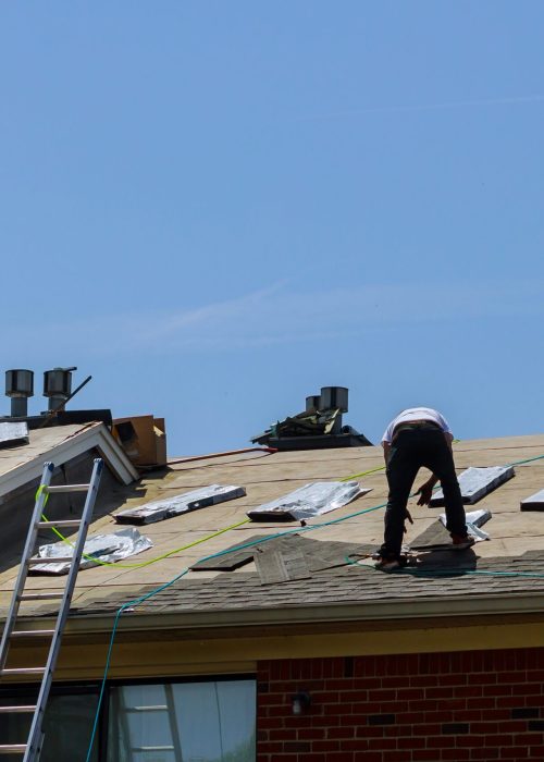 Roof repair, worker with replacing gray tiles shingles on house being applied